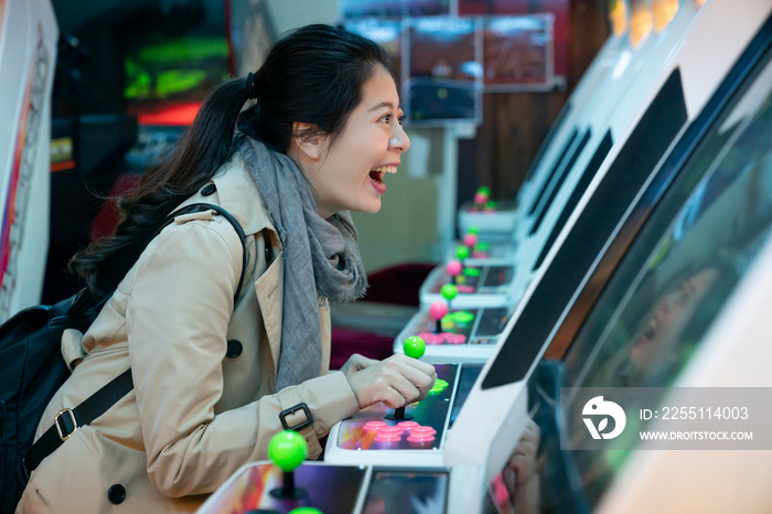 side view of excited Asian Japanese girl having fun playing arcade video games at a store in shinsekai Osaka japan. she holds the joystick of the machine and shouts in excitement