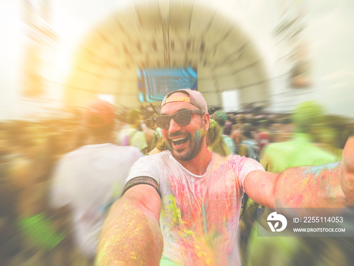 Young crazy guy taking selfie at holi powder color festival outdoor - Happy man having fun at summer fest event - Party concept - Focus on his face - Retro filter with radial defocused editing