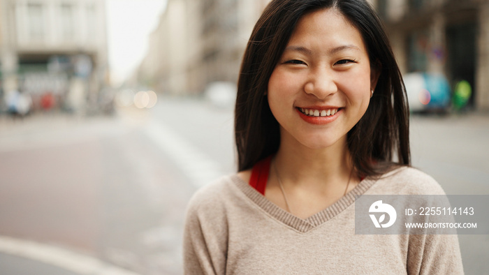 Portrait of Asian woman looking at camera smiling standing on the street. Happy emotions. City life concept