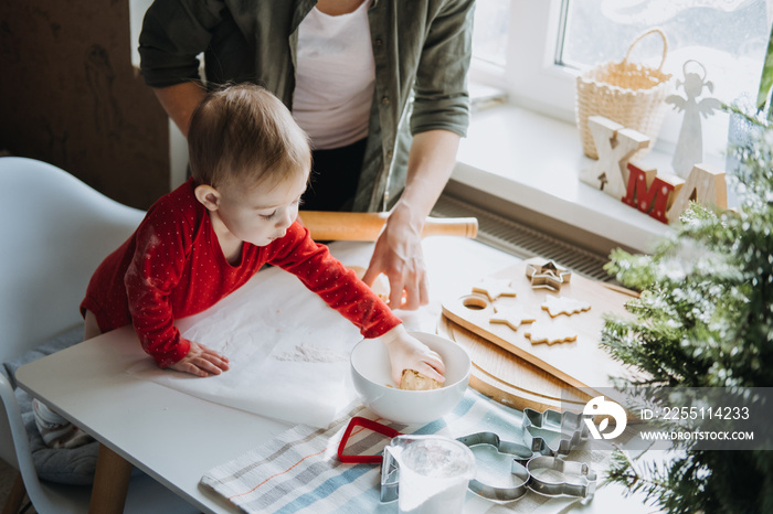 Cozy Christmas at home. Family preparation holiday dessert. Mother and baby toddler daughter play with flour, make dough and cooking gingerbread together on kitchen at home.