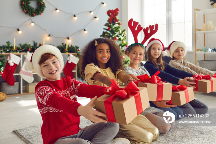 Group of happy smiling children sitting in row in living-room and holding Christmas presents