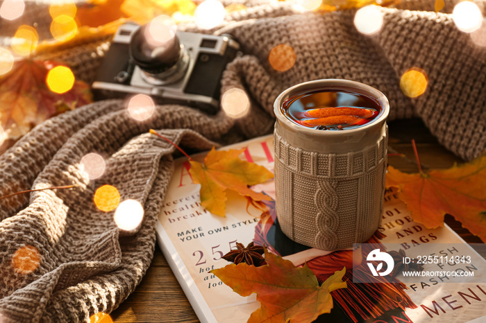 Mug of delicious mulled wine, autumn leaves, plaid and magazine on table