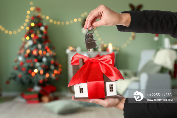 Real estate agent holding model of house and key in room decorated for Christmas. Concept of real estate