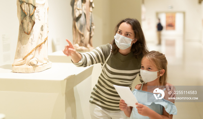 Little daughter and mother in protective masks inspect the exhibits in the museum