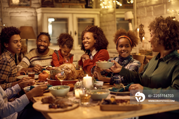 Happy black girl passing food to her grandmother during family dinner on Thanksgiving.