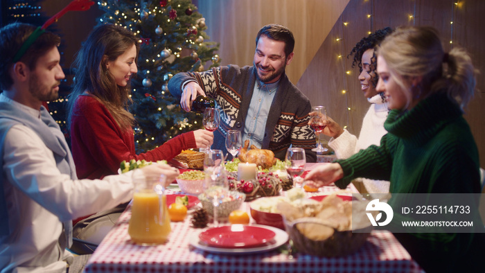 Caucasian smiling happy man host pouring wine into glasses treating his friends guests welcoming celebrating Christmas dinner and holidays together.