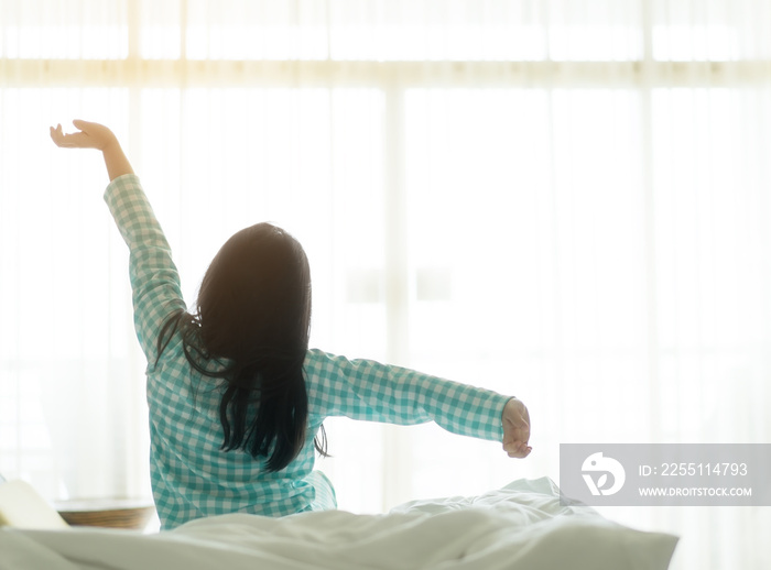 back of asian child relax or kid girl wake up or woke up with stretch oneself after sleep for waking refreshing on morning sunlight and white bed to window sheer curtain in bedroom at home on holiday