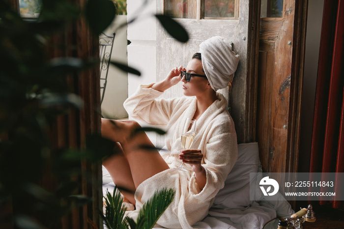 Beautiful young woman in bathrobe enjoying champagne while relaxing on the balcony