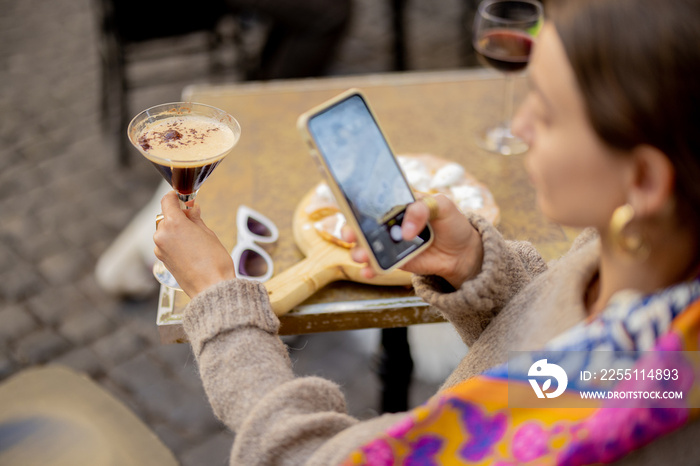 Woman taking photo of shakerato, famous coffee cocktail during a lunch with pizza at outdoor restaurant. Concept of italian cuisine and food blogging