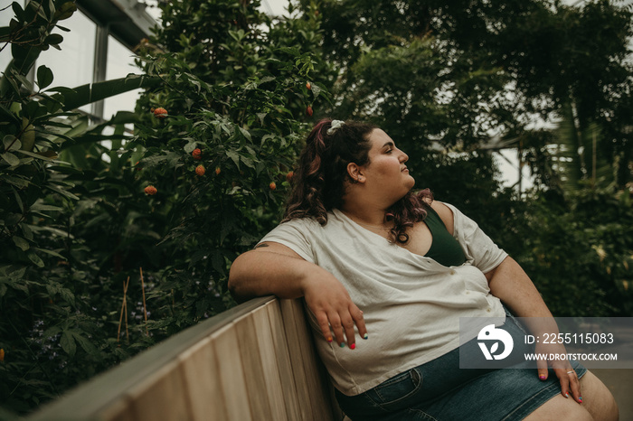 plus size woman sits on bench surrounded by plants