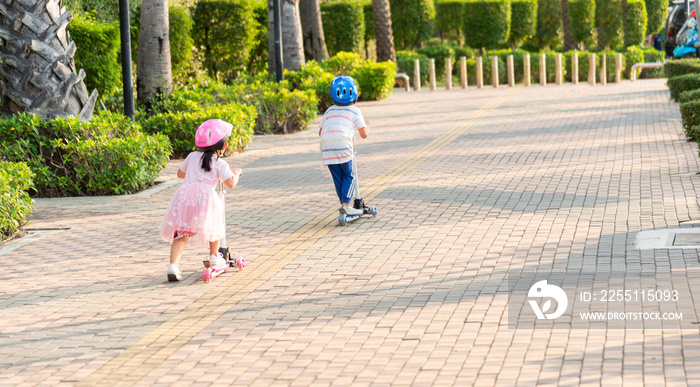 Child riding scooter. Back Asian little kid boy and girl wear safe helmet play kick board on road in park outdoors on summer day, Active children games outside, Kids sport healthy lifestyle concept