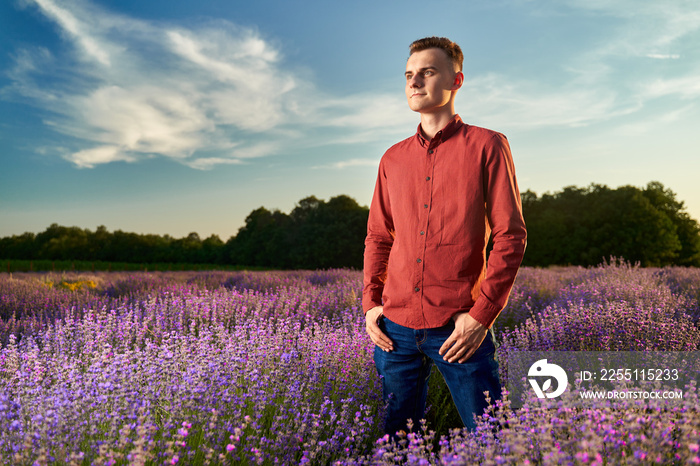 Handsome young man in red shirt and blue jeans in a lavender field at sunset