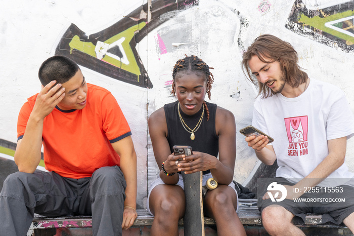 Group of young friends with skateboards using phones