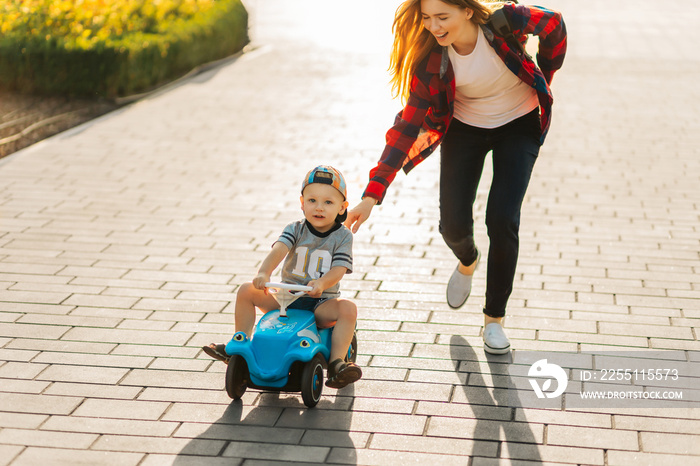 Happy cute boy riding a baby car, walking in the park with mom