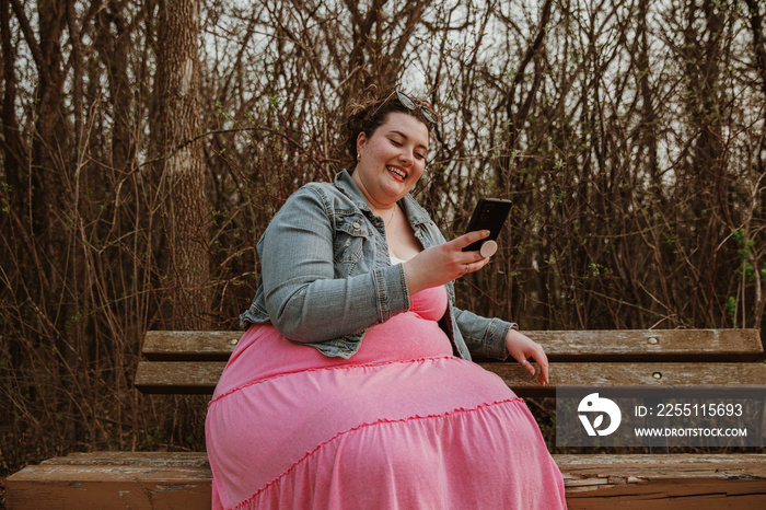 plus size woman sits on bench looking at phone