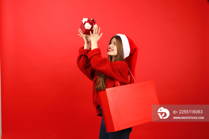 Christmas gifts and shopping. Happy young woman in santa hat tossing up holiday box on red background.