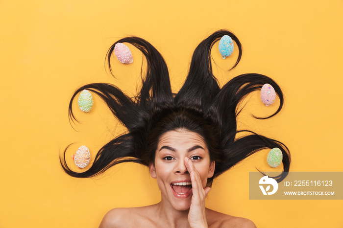 Excited young woman lies isolated on yellow background over easter eggs talking with you louder.