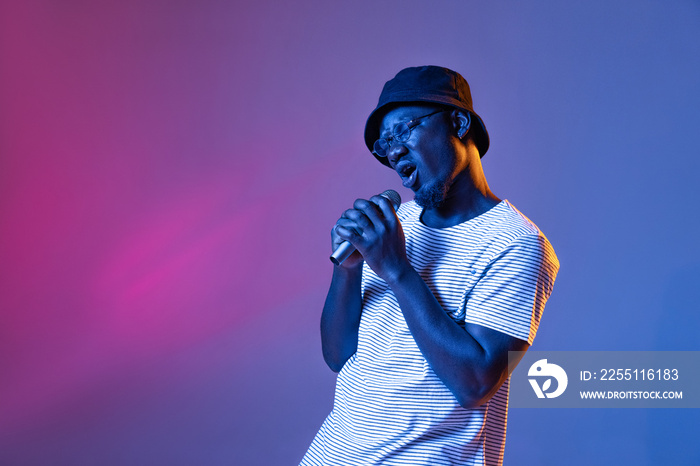 Studio shot of emotive african man with microphone isolated over gradient purple pink color studio background in neon filter