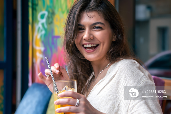 Happy young woman with a glass of lemonade against a bright painted wall.