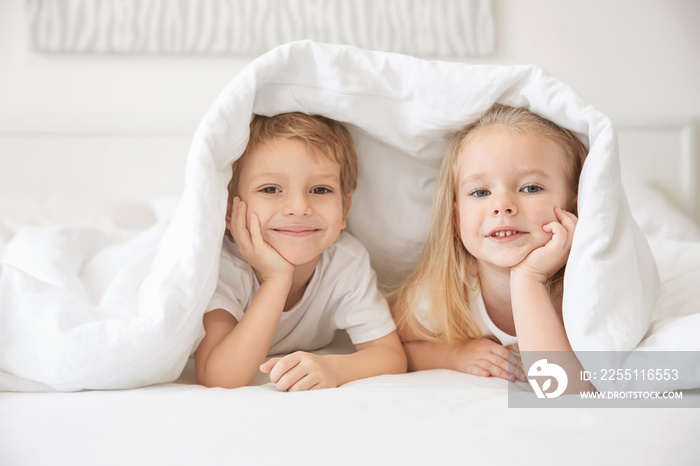 Cute children lying under blanket in bed