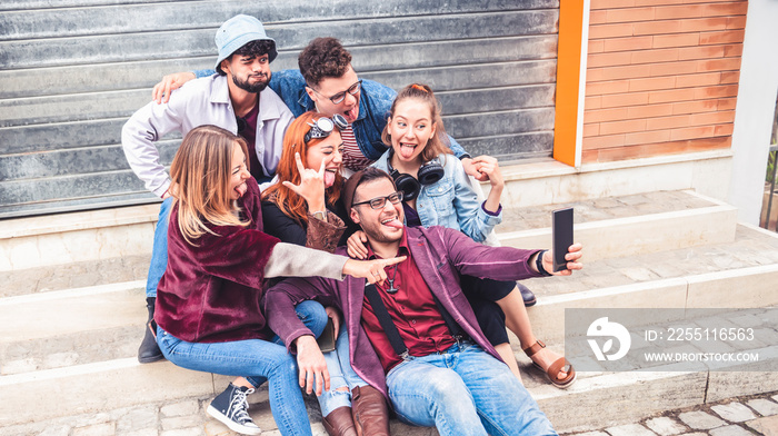 Happy millennial friends taking selfie with crazy funny faces outdoor - students take a picture sticking out their tongues sitting outside the college - friendship concept people having fun together