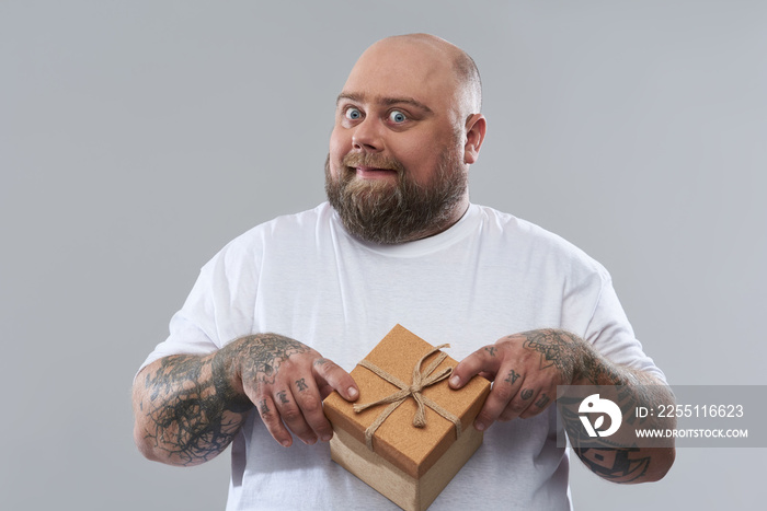 Funny bearded fat man smiling and putting gift box on his belly