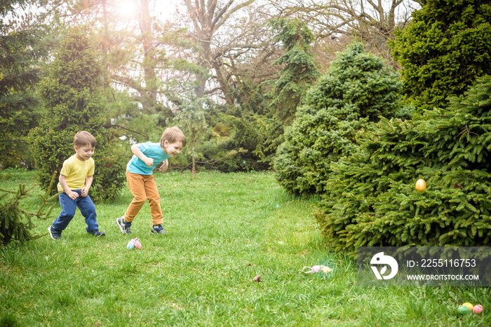 Kids on Easter egg hunt in blooming spring garden. Children searching for colorful eggs in flower meadow. Toddler boy and his brother friend kid  play outdoors