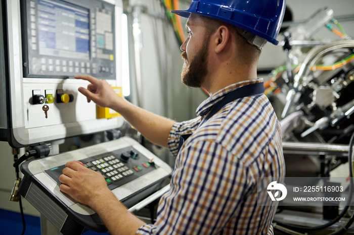 Portrait of machine operator wearing hardhat standing at control panel pressing buttons, copy space