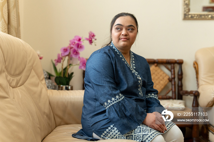 Portrait of young woman with down syndrome sitting on sofa at home