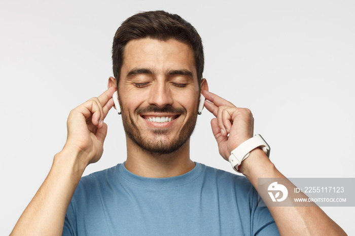 Close up shot of smiling young man in blue t-shirt listening his favourite song or cool track, feeling the rhythm and vibe with eyes closed