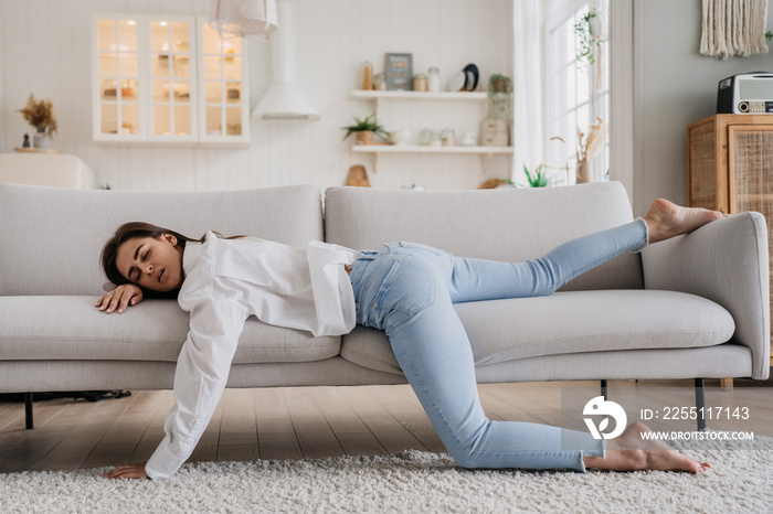 Tired woman in white shirt and blue jeans have sleeping on sofa. Tired female lying at home alone in kitchen, feels mental or physical exhaustion. Lack of energy after sleepless night, fatigue concept