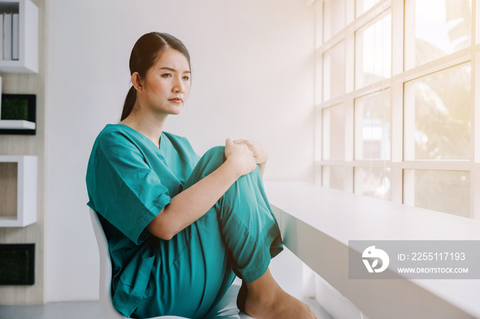 A beautiful nurse hugging her knees in a chair with a sad and worried expression, unhappy at work concept, nursing trust physician staff