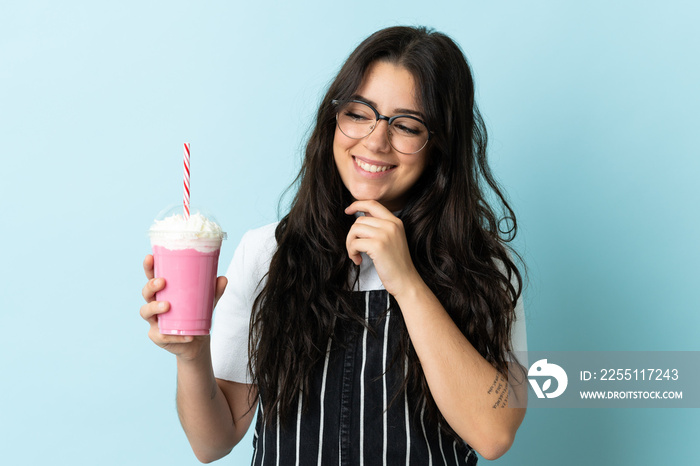 Young woman with strawberry milkshake isolated on blue background looking to the side and smiling