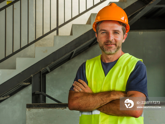 Corporate portrait of young attractive and happy builder man or constructor posing confident smiling wearing building helmet and vest in blue collar job lifestyle