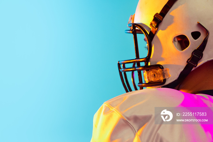 Cropped image of one American football player in sports equipment helmet and gloves isolated on blue studio background in neon light. Concept of sport, competition