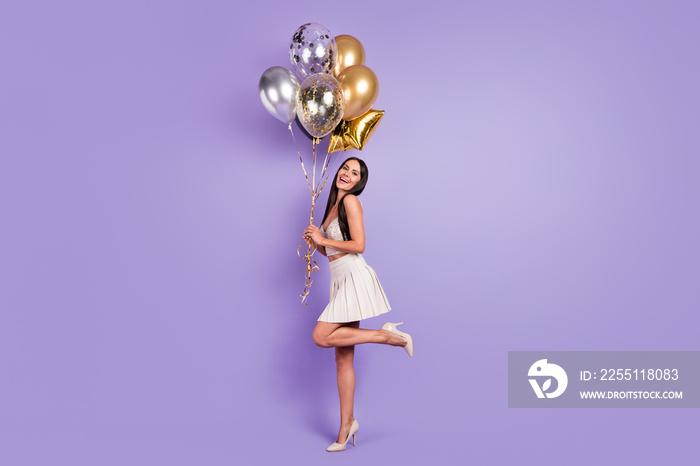 Full size profile side photo of charming happy woman hold golden balloons smile isolated on purple color background