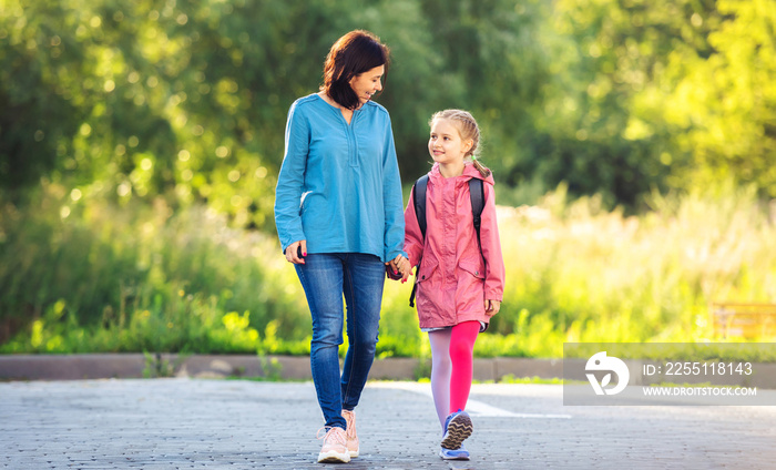 Little girl going to school with mother holding hand and smiling on sunny nature background