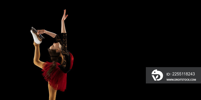 Beautiful girl, little female figure skater in beautiful stage attire skating isolated on black background in spotlight. Concept of movement, sport, beauty.