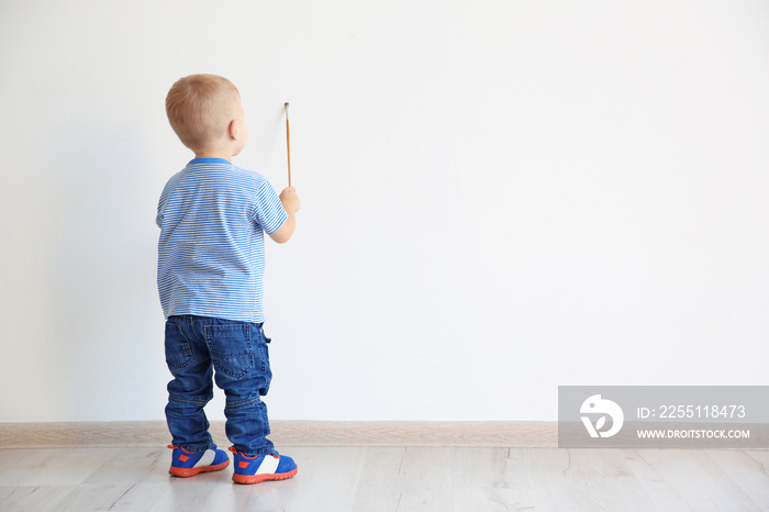 Little boy painting on white wall indoors