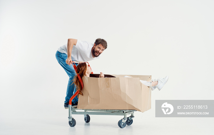 woman in a box on a cargo trolley and a cheerful male courier on a light background