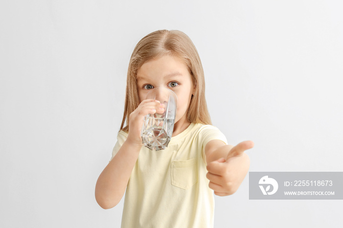 Cute little girl drinking water on light background