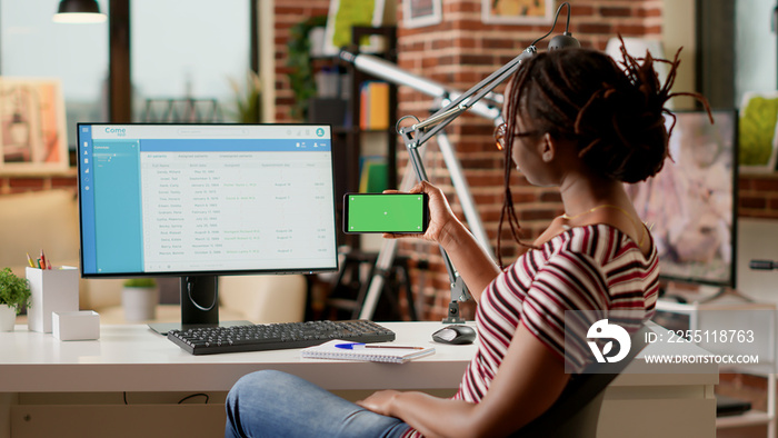 Young adult holding smartphone with horizontal greenscreen at home office desk. Looking at blank copyspace template with mockup background and isolated chroma key display. Tripod shot.