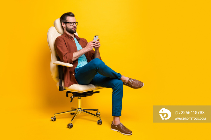 Full length body photo of serious businessman browsing internet mobile phone sitting in chair isolated bright yellow color background