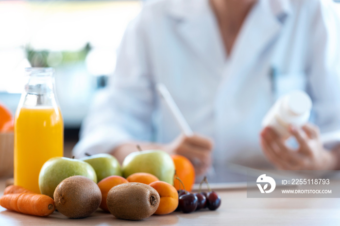 Woman nutritionist doctor writes the medical prescription for a correct diet on a desk with fruits, pills and supplements.