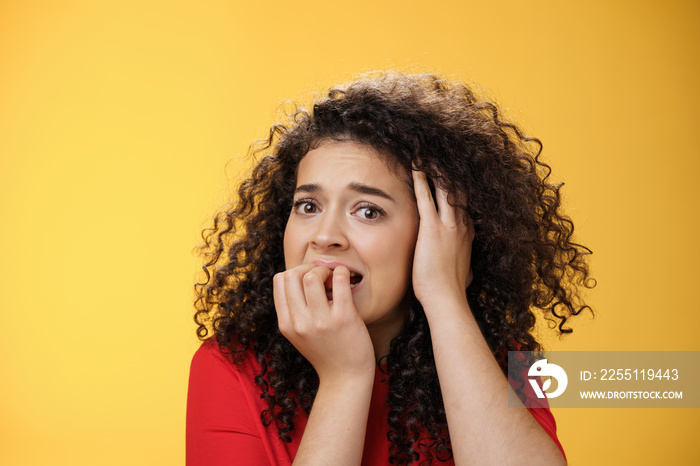 Scared woman overthinking frightened being in trouble biting fingers holding hand on head in despair, standing concerned, panicking and feeling uneasy as standing over yellow background