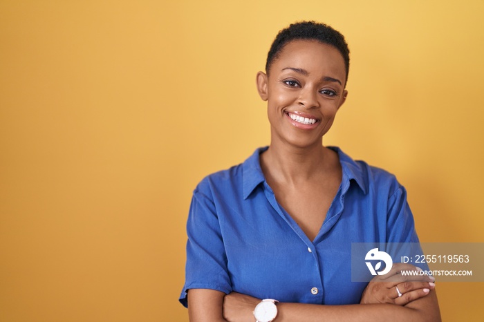 African american woman standing over yellow background happy face smiling with crossed arms looking at the camera. positive person.