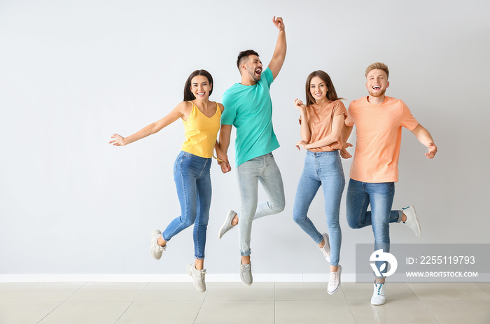 Group of jumping young people in stylish casual clothes near light wall