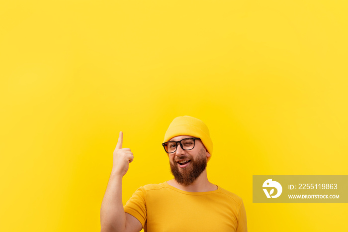 smiling bearded man with finger up, looking at camera over yellow background, advertising concept