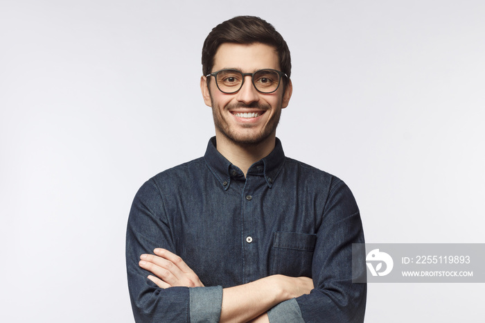 Smiling young man wearing denim shirt standing with crossed arms isolated on gray background