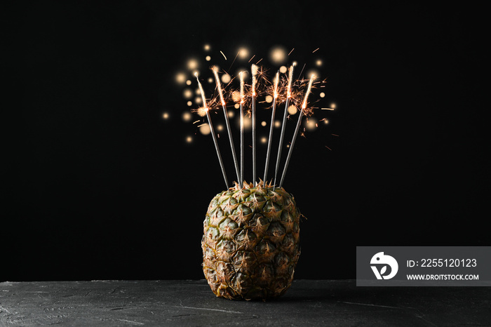 Pineapple with burning sparklers on black background, space for text